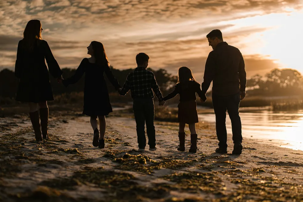 A family walking hand in hand along a beach at sunset.